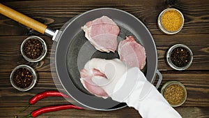 The cook puts the meat on the pan. Sliced pork steaks in a cast iron skillet. A metal frying pan on a wooden table surrounded