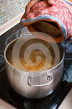 The cook puts sauerkraut from pot into saucepan