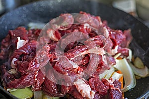 cook raw meat in a frying pan with vegetables at home.