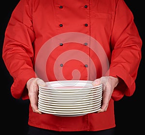 Cook in red uniform holds in his hands a stack of round white empty plates, black