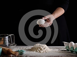 Cook`s hand on a dark background with a chicken egg. Cooking process