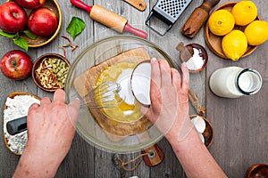 Cook's hands adding sugar to a glass bowl with a whisk, Cooking pie dough top view. Cream with eggs in glass bowl