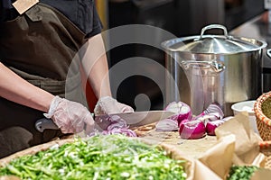 Cook's hands in cellophane gloves cutting red onion into thin slices. Cooking vegetable ingredients