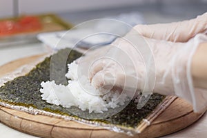 Cook's hands close-up. A chef makes sushi and rolls from rice, red fish, avocado and philadelphia cheese. step by step