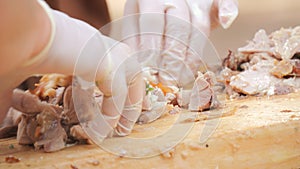 The cook's hands cut cooked pork meat into small pieces with a large knife close up view