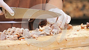 The cook's hands cut cooked pork meat into small pieces with a large knife close up view