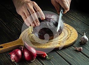 Cook's hands cut with a knife cut red cabbage on a kitchen cutting board. Cooking vegetarian food at home