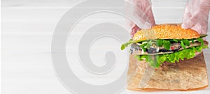 Cook`s hands lay a herring fillet sandwich with onions, cucumber and salad on paper. White wooden background with copy space for