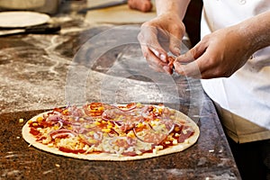 Cook`s hands putting salsiccia sausage on tomato base pizza.