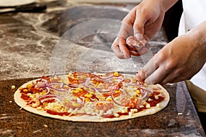 Cook`s hands putting salsiccia sausage on tomato base pizza. photo