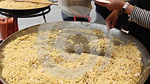 Cook serving into plates traditional Catalan pasta fideua with shrimps and mussels prepared in large paellera at street