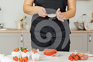 The cook sprinkles flour on a red cake through a sieve