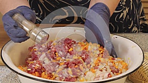 The cook sprinkles the minced meat with spices and mixes it with other ingredients in a deep metal bowl
