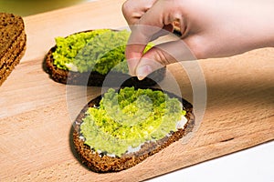 The cook sprinkles spices on a ready-made avocado sandwich. Healthy food for Breakfast, lunch or dinner. Vegetarian recipe