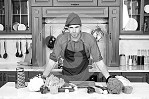 Cook stand at kitchen table. Man in chef hat and apron in kitchen. Vegetables and tools ready for cooking dishes