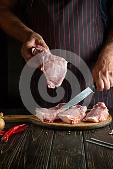 The cook with a steak in his hand in the restaurant kitchen before preparing a delicious lunch or grill. Advertising space on a