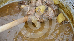 Cook stirring with wooden spoon traditional stew in kettle. Stewing meats and vegetables in enameled caldron in garden on summer