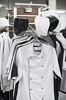 Cook uniform in a restaurant on a hanger, white and black uniforms, shirts and hats photo