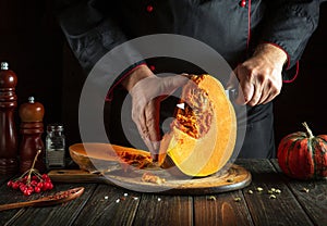 The cook uses a knife to cut a ripe pumpkin into slices on a wooden board. The concept of preparing a pumpkin dish with viburnum