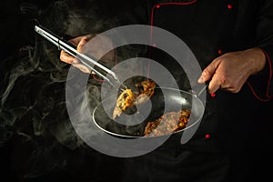 The cook uses tongs to remove hot fried fish from the frying pan. Concept of preparing a delicious fish dish in a hotel or