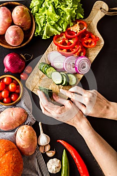 Cook vegetables. Hands cut pepper near autumn harvest on black background top-down