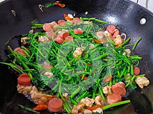 Cook vegetables kangkung with delicious sausages and tantalize your appetite against a black griddle background