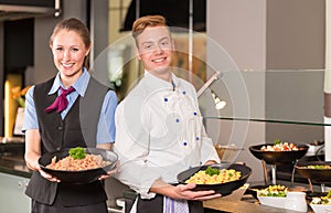 cook and waitress from catering service posing in front of buffet