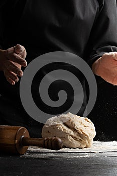 The cook works, makes the dough, kneads it in his hands on a black background. Freezing in motion. Cooking baking, culinary