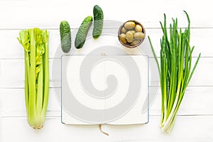 Cookbook with green fresh vegetables on white wooden background. Flat lay, eco vegan background