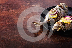 Cooked baked grilled fish, dorado, sea bream with lemon, herbs, vegetables and spices on rustic background. Top view