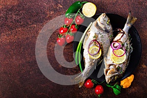 Cooked baked grilled fish, dorado, sea bream with lemon, herbs, vegetables and spices on rustic background. Top view