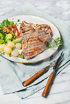 Cooked beef tbone steak with vegetables and rosemary in plate photo