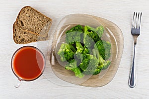 Cooked broccoli in plate, bread, cup of tomato juice