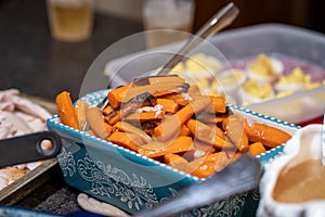Cooked carrots in a serving dish, on a table for a Thanksgiving holiday meal, in selective focus