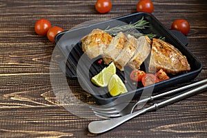 Cooked chicken breast in the oven in a grill pan. Nearby are cherry tomatoes, dry rosemary, lime, peppercorns. Dietary nutrition