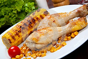 Cooked chicken thigh with a boundary of corn cob and salad