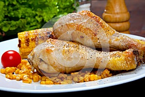 Cooked chicken thigh with a boundary of corn cob and salad