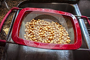 Cooked chickpeas in a drainer basket over a stainless steel sink - close-up and shallow focus