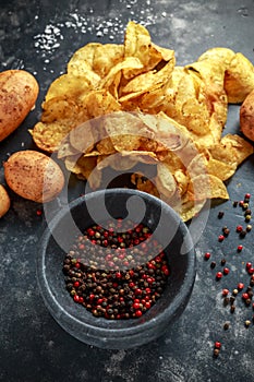 Cooked creamy peppercorn potato chips, snack crisps with sea salt on stone board with marble pestle and mortar.