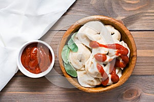 Cooked dumplings sprinkled with ketchup with arugula leaves in a wooden plate and a bowl of ketchup on the table