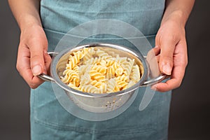 Cooked fusilli pasta in a sieve or strainer, italian food ingredients, hands holding colander