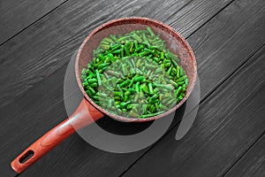 Cooked green beans in a frying pan on a black wooden background. Space to copy. Top view