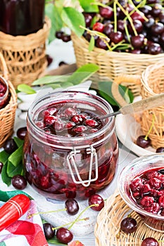 Cooked homemade cherry jam in glass jar on white wooden table outdoors, fresh cherry jam close up