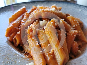 Cooked Italian pasta under vegetables and tomato paste in a plate on a black wooden table. Traditional cuisine