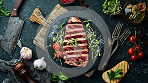 Cooked juicy tuna steak with vegetables on a black stone plate. Restaurant food. Seafood. Rustic style.