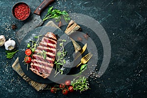 Cooked juicy tuna steak with vegetables on a black stone plate. Restaurant food. Seafood. Rustic style