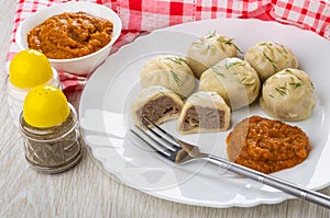 Cooked khinkali, squash caviar, fork in plate, salt, pepper, napkin on wooden table