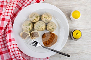 Cooked khinkali, squash caviar, fork in plate, salt, pepper, napkin on wooden table. Top view