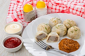 Cooked khinkali, squash caviar, fork in plate, salt, pepper, sauces in bowls, napkin on wooden table