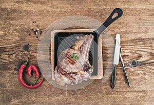 Cooked meat rib eye steak with spices, red chili, rosemary and vintage silverware incookinf pan over rustic wooden